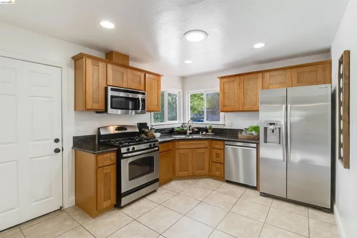Kitchen featuring stainless steel appliances, wood cabinetry, dark countertops, and tile flooring