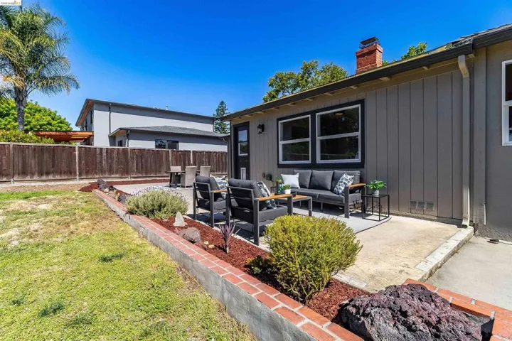 Rear exterior featuring a concrete patio, board and batten siding, multiple windows, and a brick chimney
