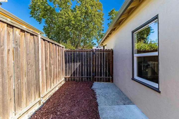 Side yard with a wood fence, a gravel and concrete path, and a window with dark trim on a stucco exterior