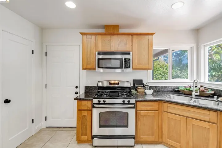 Kitchen featuring honey-toned cabinetry, stainless steel appliances, dark stone countertops, and a dual basin sink