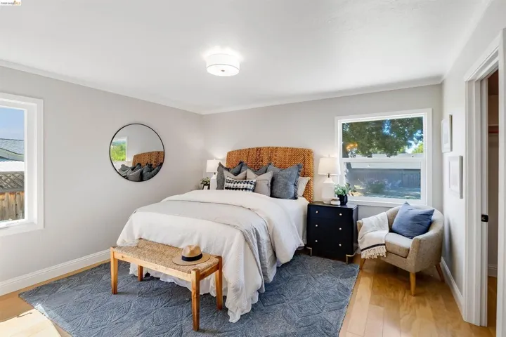 Light-filled room featuring wood-finish flooring, two windows, a ceiling-mounted light fixture, and crown molding