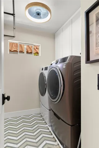 Chevron marble/porcelain mosaic tile floor and white shaker upper cabinets with soft close doors above washer/dryer
