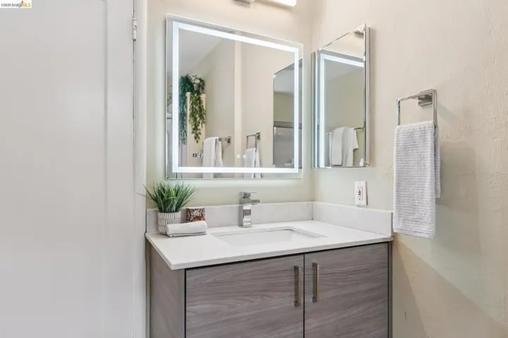 Modern vanity featuring a single basin, light-colored countertop, and wood-finish cabinetry with silver-toned hardware