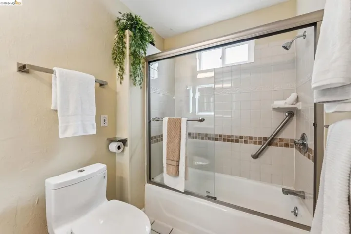 Bathroom featuring a white toilet, brushed nickel towel bar, and a tub/shower combination with sliding glass doors