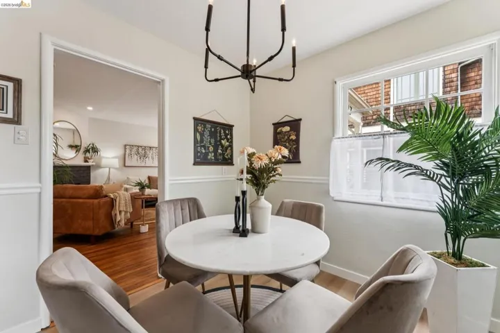 Dining area featuring a white marble-look round table, light wood-finish flooring, a contemporary black chandelier, and a framed doorway opening to an adjacent room with wood flooring