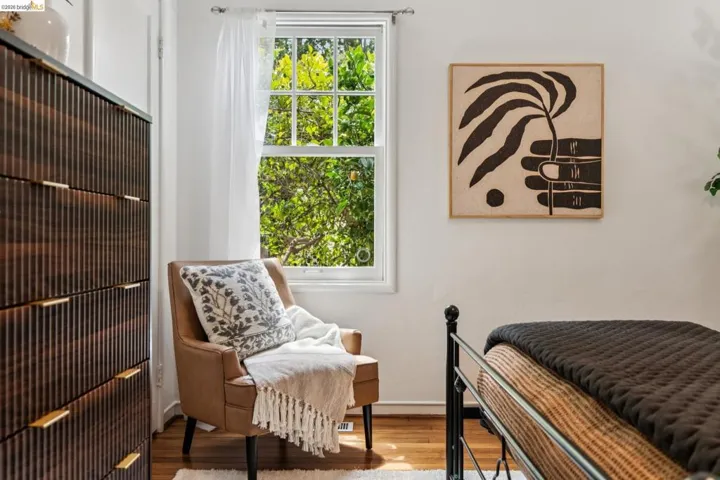 Hardwood flooring featuring a window with abundant natural light, a wood-finish dresser with gold-tone hardware, and white walls