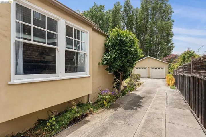 Detached two-car garage with dual pane windows, a concrete driveway, and an adjacent garden bed with established plantings