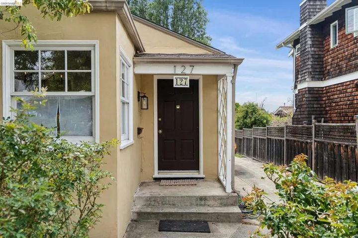 Stucco exterior with a covered entry, dark paneled front door, white trim windows, and a concrete pathway with a wooden fence