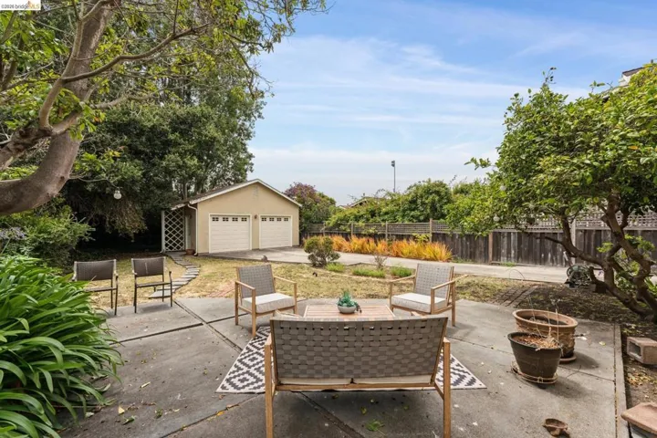 Expansive concrete patio area with mature trees and perimeter landscaping