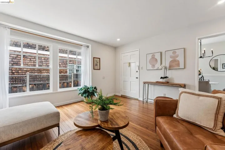Sunlit living room featuring rich wood-finish flooring, recessed lighting, and a paneled entry door