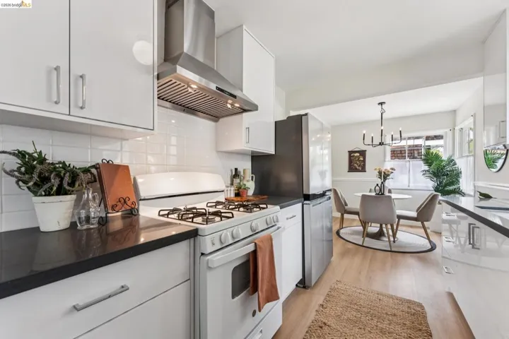 Kitchen featuring white cabinetry, dark countertops, a stainless steel range hood, white subway tile backsplash, and light wood-finish flooring