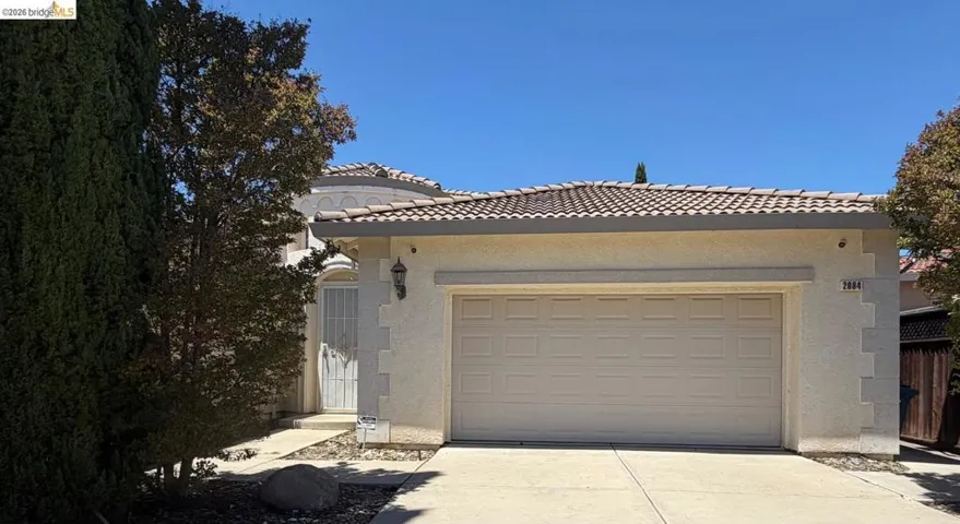 Stucco exterior featuring a two-car garage, concrete driveway, and mature landscaping