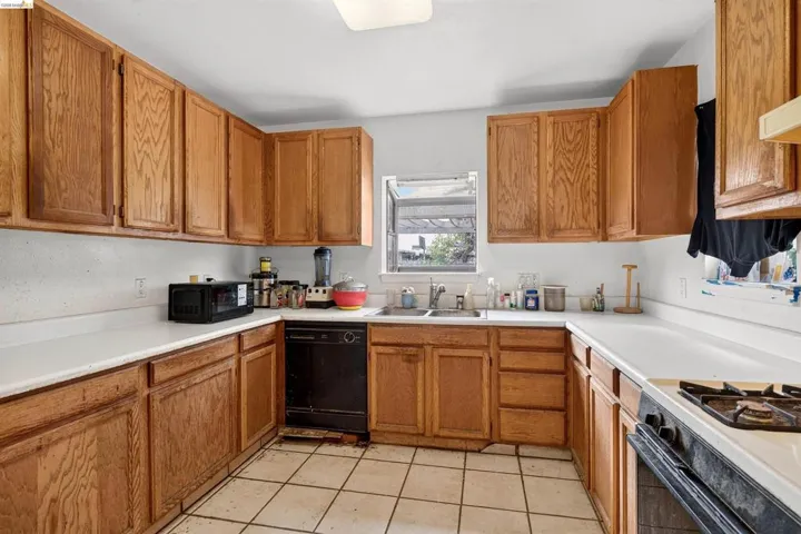 U-shaped kitchen featuring wood cabinetry, white countertops, tile flooring, and a window above the sink