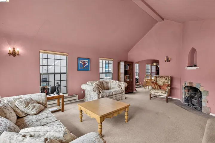 Vaulted ceiling living area featuring a stone-surround fireplace, carpeted flooring, and multiple grid-pattern windows