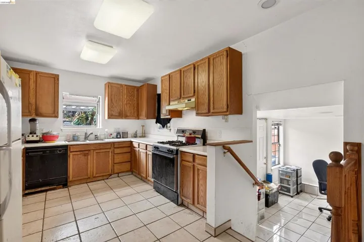 L-shaped kitchen featuring wood cabinetry, white countertops, a window over the sink, and tile flooring