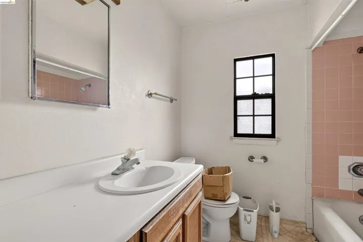 Bathroom featuring a single-sink vanity with wood-finish cabinetry, a window with black trim, and pink tiled bath surround