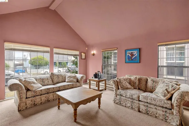 Spacious living area featuring a vaulted ceiling, multiple large windows, and wall-to-wall carpeting