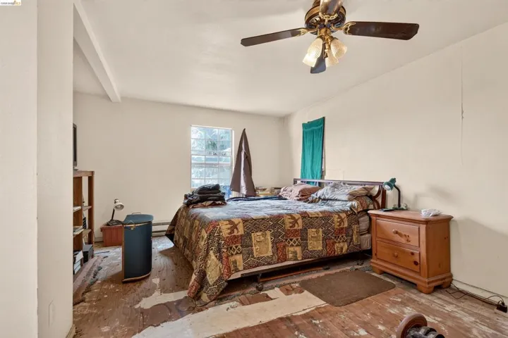Bedroom featuring an angled ceiling with exposed beam, a window with glass block accents, a ceiling fan with integrated lighting, and wood-finish flooring