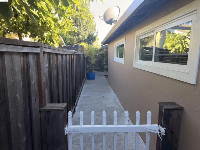 Side yard access featuring a concrete pathway, wood privacy fencing, and a white picket gate