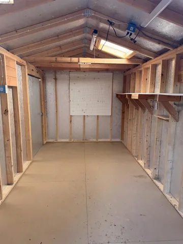 Storage shed interior featuring exposed wooden framing, a skylight, overhead fluorescent lighting, and a metal pegboard