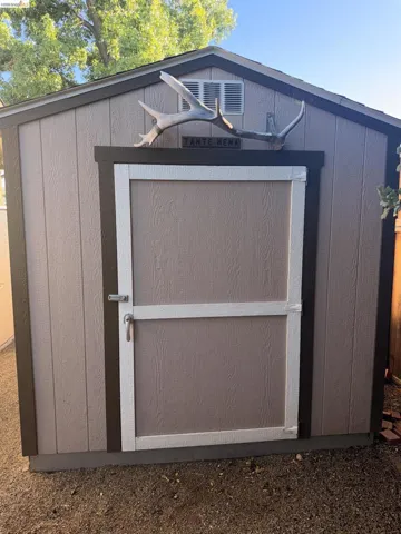 Utility shed featuring vertical panel siding, a gable roof, and a single entry door with a white trim surround