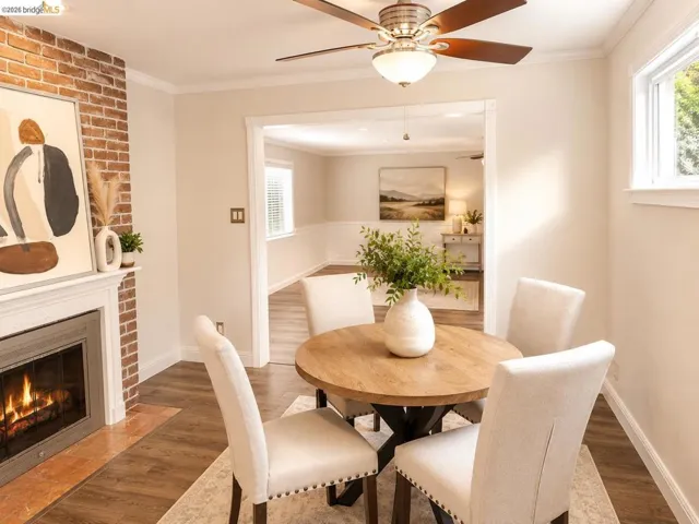 Dining area featuring wood-finish flooring, a brick-faced fireplace with a white mantel, and a ceiling fan with integrated lighting