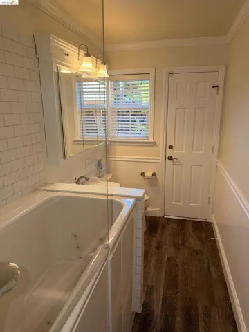 Bathroom featuring a white jetted bathtub with a clear glass shower panel, subway tile surround, wood-finish flooring, and a window with white blinds