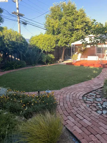 Expansive backyard featuring a manicured lawn, a curved brick pathway, a privacy fence, mature trees, and a raised wooden deck with a white gazebo