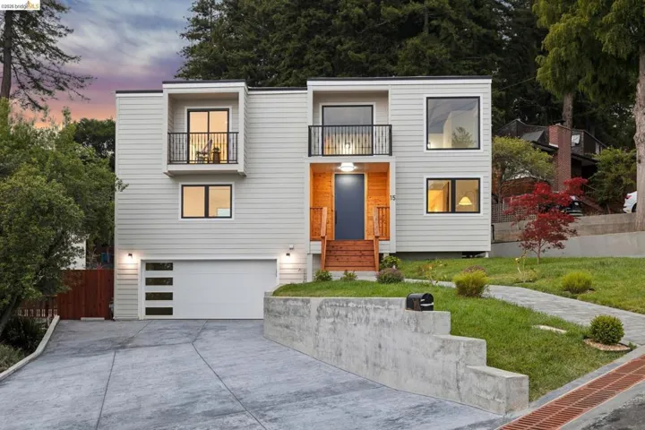 Contemporary multi-level residence featuring horizontal siding, a two-car garage with frosted glass panels, and multiple balconies with dark iron railings