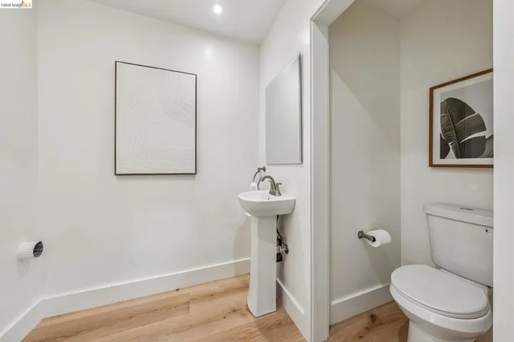 Compact powder room featuring a pedestal sink with a brushed nickel faucet, a white toilet, recessed lighting, and wood-finish flooring