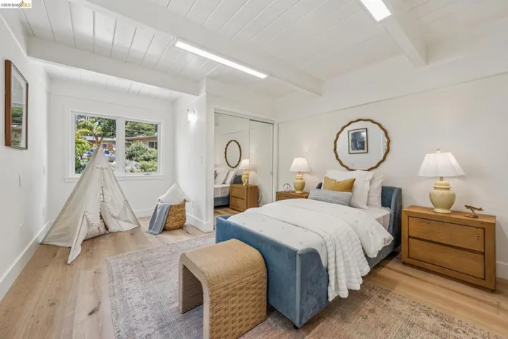 Bright bedroom featuring wood-finish flooring and a white paneled ceiling with exposed beams