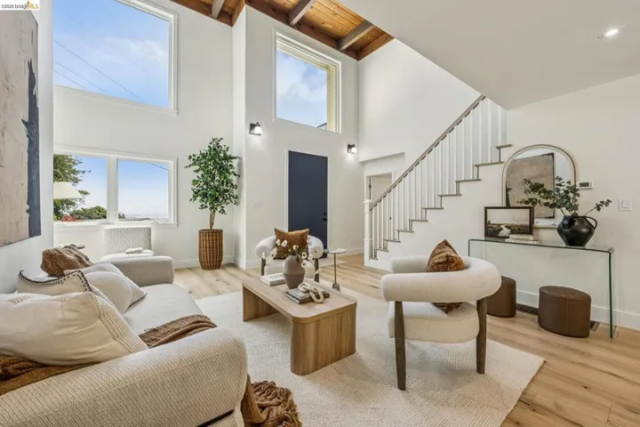 Living area featuring high ceilings with exposed wood beams, multiple large windows, and light wood-finish flooring