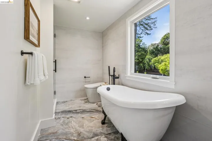 Freestanding soaking tub with dark-finish fixtures, large window, and patterned stone-finish floor