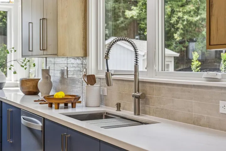 Kitchen countertop featuring an undermount double-basin sink with a commercial-style pull-down faucet, a white solid surface countertop, and a tiled backsplash
