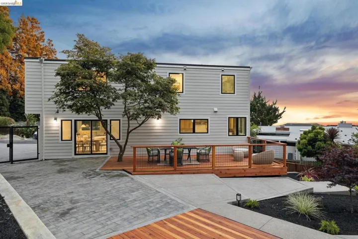 Contemporary two-story exterior featuring light gray siding with black-framed windows, a multi-level wood deck with cable railing, and sliding glass doors