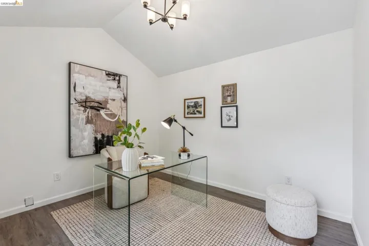 Vaulted ceiling room featuring wood-finish flooring, a contemporary chandelier, white baseboards, and bright white walls