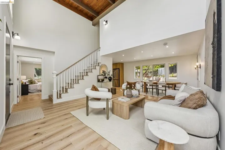 Expansive living area with vaulted wood-paneled ceilings, light wood-finish flooring, a white spindle staircase with wood handrail, recessed lighting, and large windows