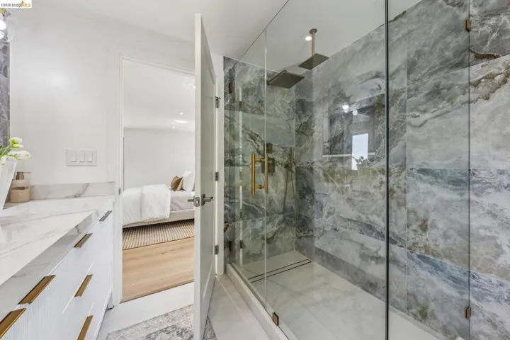Glass-enclosed shower featuring natural stone-patterned tile, multiple shower heads, and gold-finish fixtures