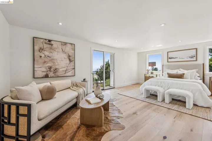 Spacious bedroom featuring light wood-finish flooring, recessed lighting, expansive glass doors leading to a balcony, and multiple large windows