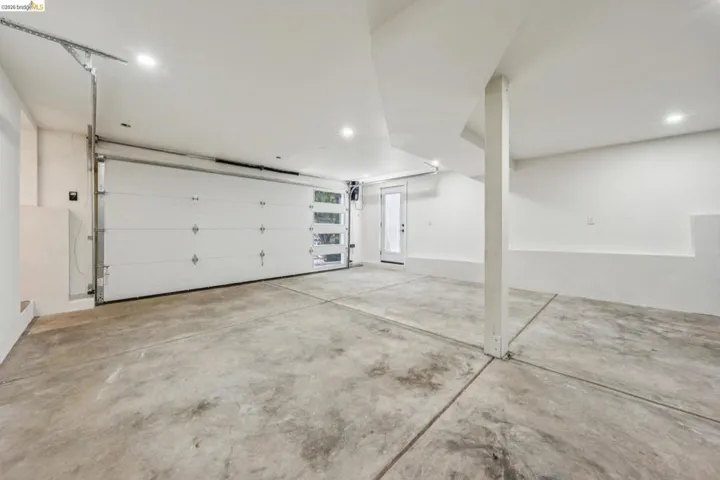 Spacious garage featuring a modern sectional overhead door with frosted glass panels, concrete flooring, recessed lighting, and a white paneled entry door