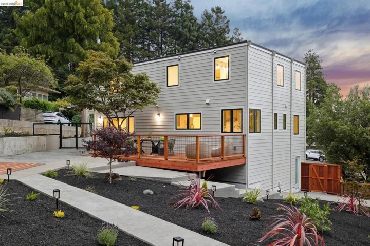 Modern multi-level exterior with light gray siding, black-framed windows, and a wood deck featuring a cable railing