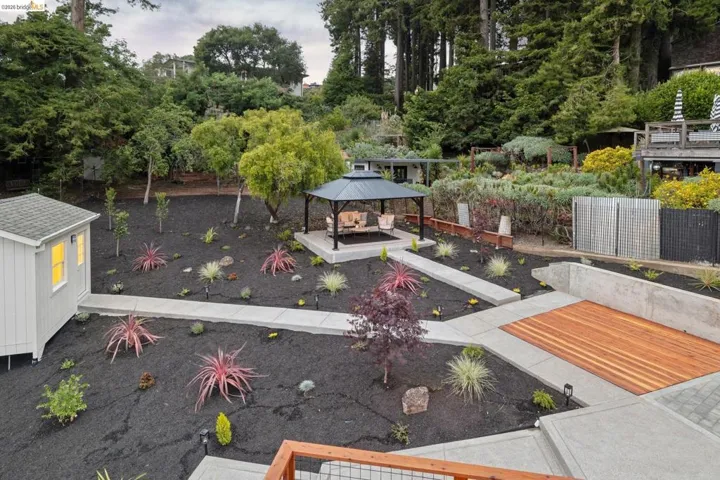 Landscaped backyard featuring a gazebo, detached outbuilding, concrete pathways, and a wood-finish deck section
