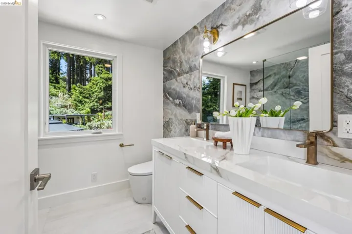 Bathroom featuring a double vanity with white cabinetry and gold-toned hardware, topped with a white countertop and integrated sinks