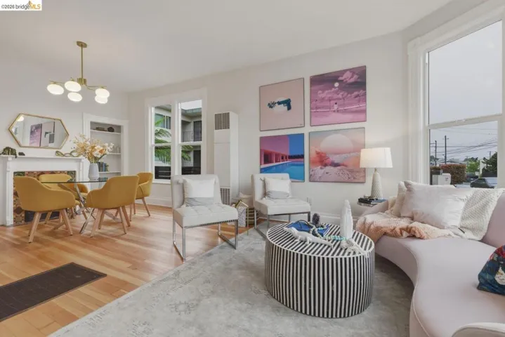 Open-concept living space featuring wood-finish flooring, a decorative fireplace with a white mantel, built-in shelving, large windows with white trim, and recessed wall features
