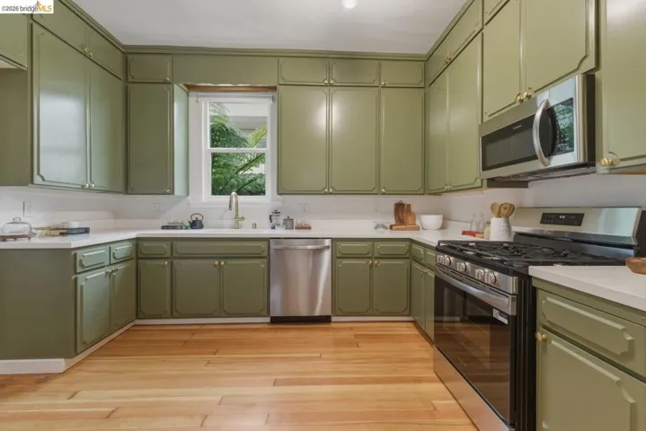 U-shaped kitchen featuring extensive green cabinetry, white countertops, stainless steel appliances, a tile backsplash, and light wood-finish flooring