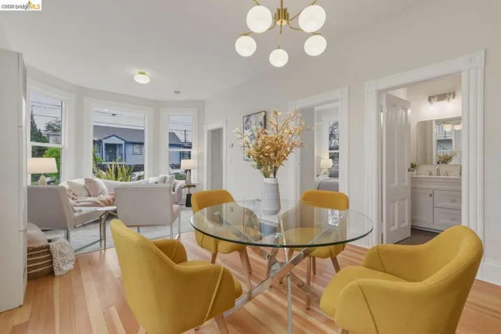 Hardwood flooring spans the open-concept room, featuring a bay window, a modern chandelier, and a doorway to a bathroom with a dual vanity