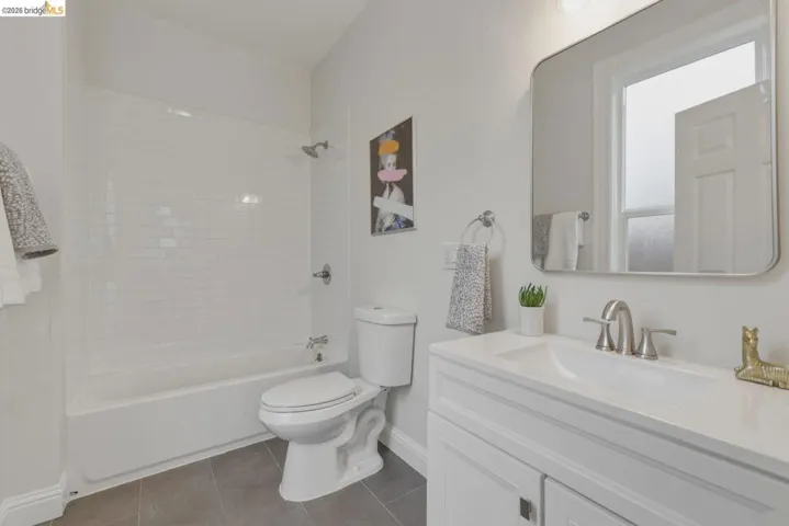 Bathroom featuring a white subway tile shower surround, a white vanity with an integrated sink, a rectangular framed mirror, and grey tile flooring