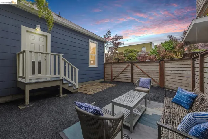 Outdoor patio area featuring dark aggregate surfacing, a light wood privacy fence, and a raised exterior door with a landing and railings