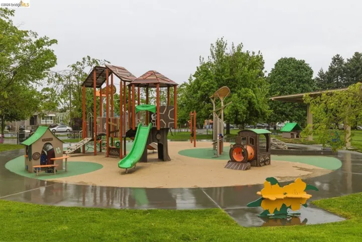 Community playground with multiple play structures, a train-themed feature, green slides, and soft fall surfacing