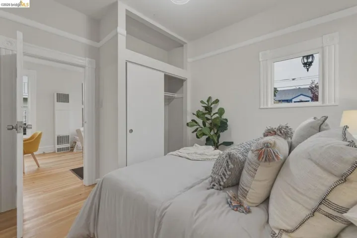 Bedroom featuring wood-finish flooring, a window with decorative trim, and an integrated closet with sliding doors and overhead shelving